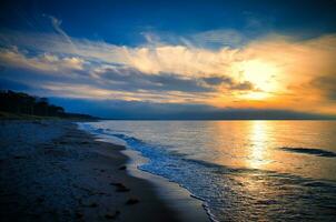 le coucher du soleil sur le Ouest plage sur le baltique mer. vagues, plage, nuageux ciel et ensoleillement photo