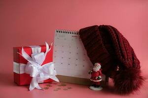 cadeau boîte et calendrier avec une rouge tricoté la laine chapeau sur rose Contexte. Noël journée concept. Planification Planification ordre du jour, événement, organisateur Noël journée. photo