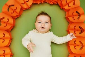 Halloween portrait de adorable bébé mensonge sur vert Contexte suivant à citrouille guirlande photo