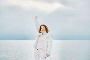 Extérieur portrait de magnifique femme portant blanc veste, relaxant suivant à Lac ou mer photo