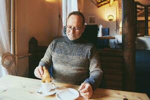 intérieur portrait de Sénior homme en buvant Matin café avec croissant photo