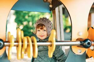 Extérieur portrait de content souriant bambin fille ayant amusement sur Cour de récréation, du froid temps photo