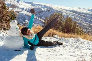 hiver récréation latina femme ayant amusement suivant à bonhomme de neige dans neigeux scène photo