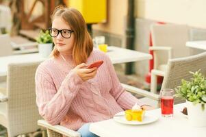 Extérieur portrait de mignonne Jeune adolescent fille repos dans café, écoute la musique ou Podcast photo