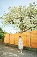 Extérieur maternité portrait de content Jeune Enceinte femme permanent suivant à épanouissement arbre, printemps photo