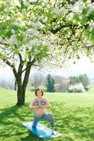 Extérieur portrait de content Jeune Enceinte femme pratiquant youga dans printemps jardin en dessous de épanouissement Pomme des arbres, en bonne santé mode de vie photo