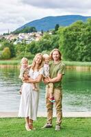 Extérieur portrait de magnifique famille, Jeune couple avec enfant d'âge préscolaire garçon et bambin fille posant suivant à Lac ou rivière photo