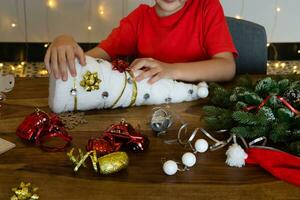 le garçon est séance à le table à maison. une enfant fait du une blanc Noël arbre par lui-même, artisanat. DIY. Noël décorations photo