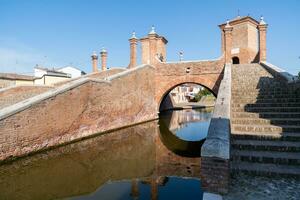 comacchio ,Italie-juin 2, 2023-personnes promenade dans comacchio dans de face de le célèbre Trois des ponts pendant une ensoleillé journée photo