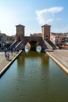 comacchio ,Italie-juin 2, 2023-personnes promenade dans comacchio dans de face de le célèbre Trois des ponts pendant une ensoleillé journée photo