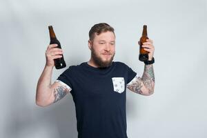 brutal barbu Masculin avec tatoué bras les boissons une Bière de une bouteille. photo