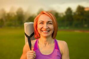 magnifique femme souriant avec une yoga tapis sur le Contexte de le parc. photo