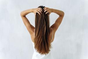 beauté et soin des cheveux. taille jusqu'à l'arrière portrait d'une jeune femme brune aux cheveux volumineux lissants en y touchant avec ses mains. isolé sur blanc photo