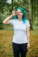 Jeune femme avec turquoise teint cheveux dans blanc t chemise détient Fait main coloré œil talisman photo