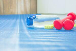 un pomme, deux rouge haltères et une bouteille de l'eau sur une bleu tapis. Accueil faire des exercices concept photo