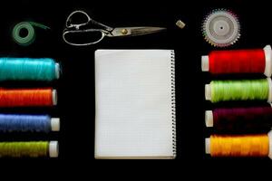 multicolore fils, ruban mesure, ciseaux, épingles et bloc-notes pour Remarques sur une noir Contexte. vue de au-dessus de. photo