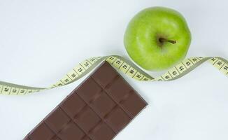 choisir entre une en bonne santé mode de vie et déchet aliments. Pomme centimètre ruban et Chocolat sur une blanc Contexte photo