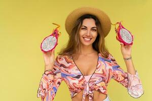 magnifique européen femme dans élégant été tenue et paille chapeau posant sur Jaune Contexte. mode regarder. en portant tropical des fruits. photo