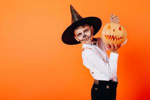 portrait de garçon en maquillage mascarade diable et chapeau montrant une citrouille. concept d'halloween photo