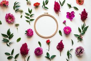 gros plan de fleurs fraîches et de feuilles vertes éparpillées sur un fond blanc. espace de copie de cercle au centre photo