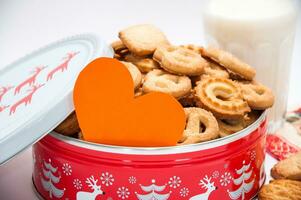 Orange papier cœur dans le métal boîte avec Noël biscuits et verre de Lait sur le Contexte photo