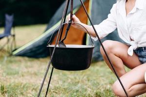 Jeune femme cuisinant dans le camping assis à côté du feu de joie - image de recadrage photo