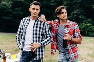 deux gars tenant une bière et debout dans le camping. - image photo