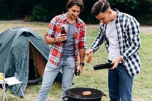 deux gars cuisinent des saucisses sur le barbecue du camping. - image photo