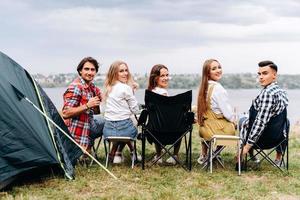 une compagnie d'amis s'amuse au camping. ils sont assis un demi-tour. - vue arrière photo