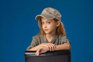 peu fille dans une casquette avec gris yeux et blond cheveux séance sur une chaise photo