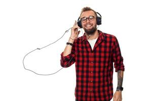 Jeune branché homme dans à carreaux chemise et des lunettes portant écouteurs à la recherche content sur blanc Contexte. photo