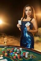 Jeune magnifique femme pose près poker table dans luxe casino. passion, cartes, puces, alcool, dé, jeu, casino - il est comme femelle divertissement. fumée Contexte. photo
