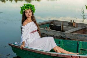 Jeune femme avec fleur couronne sur sa diriger, relaxant sur bateau sur rivière à le coucher du soleil. concept de femelle beauté, du repos dans le village photo