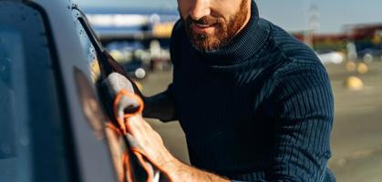 vue recadrée d'un jeune homme heureux polissant sa voiture avec un chiffon en microfibre tout en se sentant satisfait pendant la journée d'été ensoleillée. stock photo