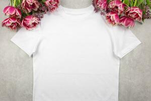 blanc aux femmes coton T-shirt maquette avec rose tulipes fleurs sur gris béton Contexte. conception t chemise modèle, impression présentation moquer en haut. Haut vue plat poser. photo