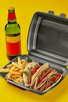 Birria tacos dans à emporter récipient avec frites et bouteille de boisson sur Jaune Contexte photo