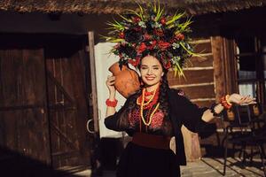 brunette fille dans une noir et rouge ukrainien brodé authentique nationale costume et une couronne de fleurs est posant permanent à le portail. photo