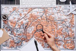 une carte est disposée sur une table en bois, un homme regarde quelque chose à partir d'une loupe, d'une boussole, d'un cahier et d'un stylo photo