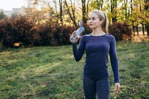 remise en forme dans le parc, la fille tient une bouteille d'eau à la main. photo