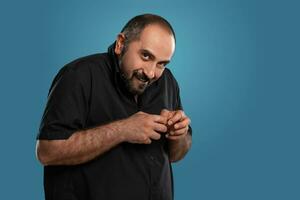 fermer portrait de une brunet âge moyen homme avec barbe, habillé dans une noir T-shirt et posant contre une bleu Contexte. photo