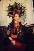 brunette fille dans une blanc ukrainien authentique nationale costume et une couronne de fleurs est posant contre une terrasse. fermer. photo