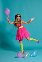 charmant fille avec une multicolore tresses coiffure et brillant se maquiller, posant dans studio avec air des ballons contre une bleu Contexte. photo