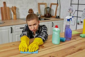 Jeune femme dans protecteur gants lingettes une table dans le cuisine avec une chiffon photo
