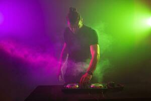 dj à travail mélange du son sur sa ponts à une fête ou nuit club avec coloré fumée lumière Contexte photo