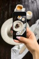 photographier nourriture concept - femme prend image de magnifique décoré Chocolat gâteau avec d'or des noisettes et une tasse de café photo