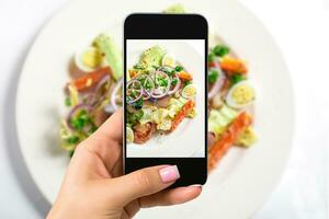 photographier nourriture concept - femme prend image de Frais salade avec laitue, œufs, tomates, oignon anneaux, poivrons photo