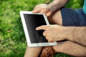 Jeune branché garçon séance dans le parc et en utilisant moderne numérique tablette photo