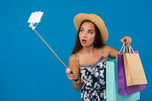 Jeune élégant femme posant et prise une selfie sur le téléphone avec achats Sacs sur une bleu Contexte photo