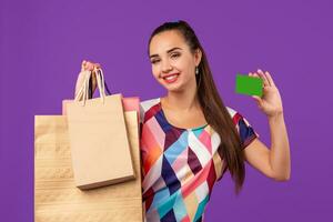 attrayant femme Années 20 dans robe en portant achats paquets et montrant vert crédit carte isolé plus de violet Contexte photo