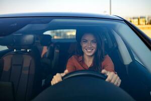 content femme conduite une voiture et souriant. mignonne Jeune Succès content brunette femme est conduite une auto. portrait de content femelle chauffeur pilotage voiture avec sécurité ceinture photo